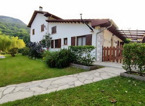 Une maison à deux étages, avec un chemin de pierre menant à l’entrée, entourée de verdure et délimitée par une clôture en bois.