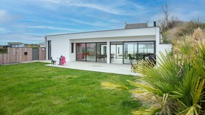 A modern house with a large glass door, a patio with outdoor furniture, and a well-maintained lawn. - Villa 'Ker Marie' with Sea View, Private Terrace and Wi-Fi (Locquirec)
