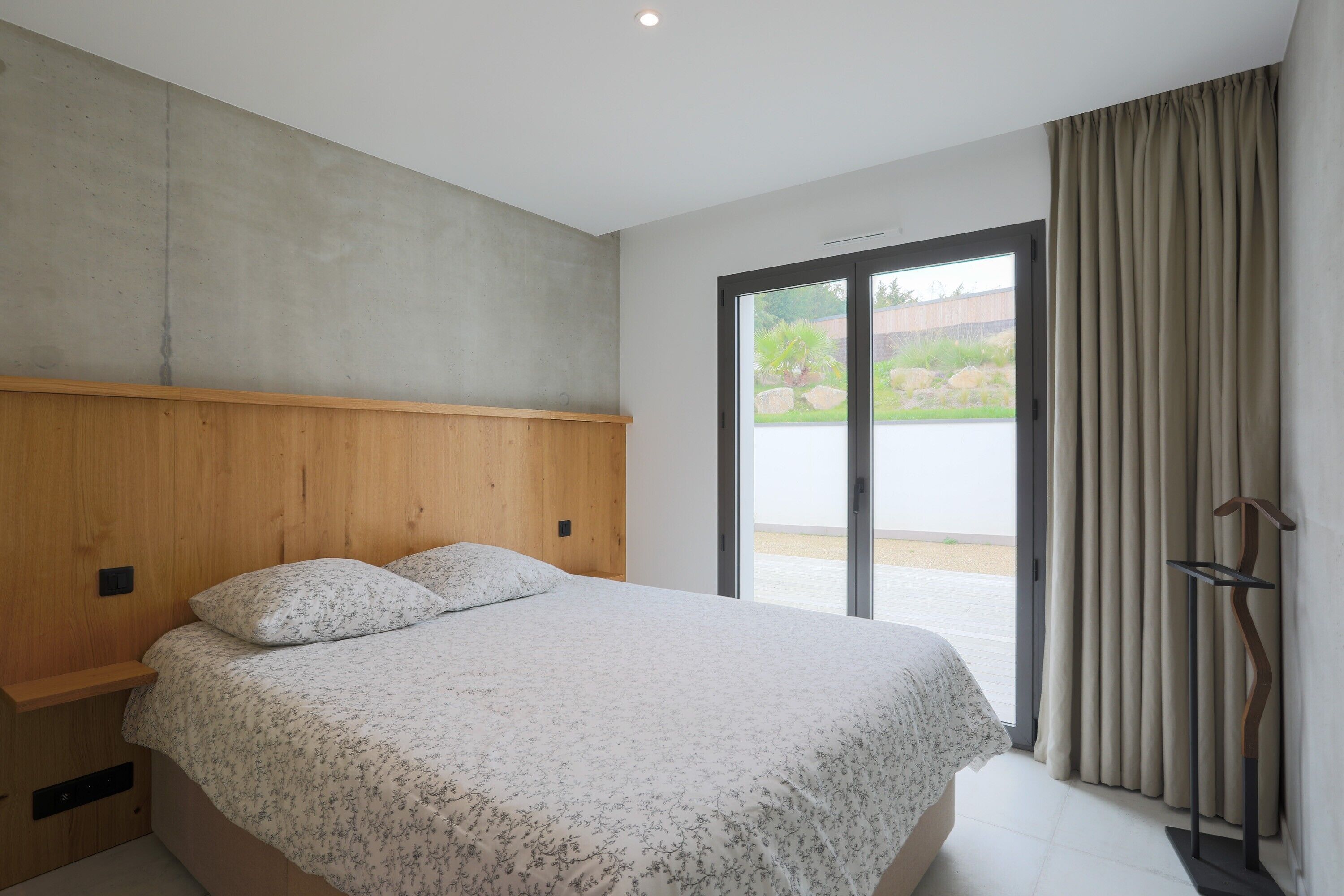 A bedroom with a bed, wooden headboard, and a view through a sliding door to an outdoor area.