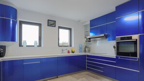 A modern kitchen with blue cabinets, a built-in oven, and a window. - Villa 'Ker Louise' with Sea View, Shared Terrace and Wi-Fi (Locquirec)