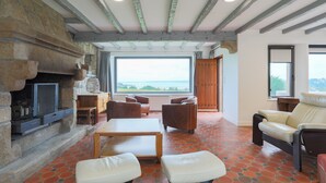 A spacious living area with a stone fireplace, comfortable seating, and a large window offering a view. - Villa 'Ker Louise' with Sea View, Shared Terrace and Wi-Fi (Locquirec)