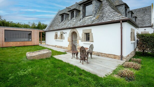 A white building with a stone roof, a wooden deck, and a stone bench. - Villa 'Ker Louise' with Sea View, Shared Terrace and Wi-Fi (Locquirec)