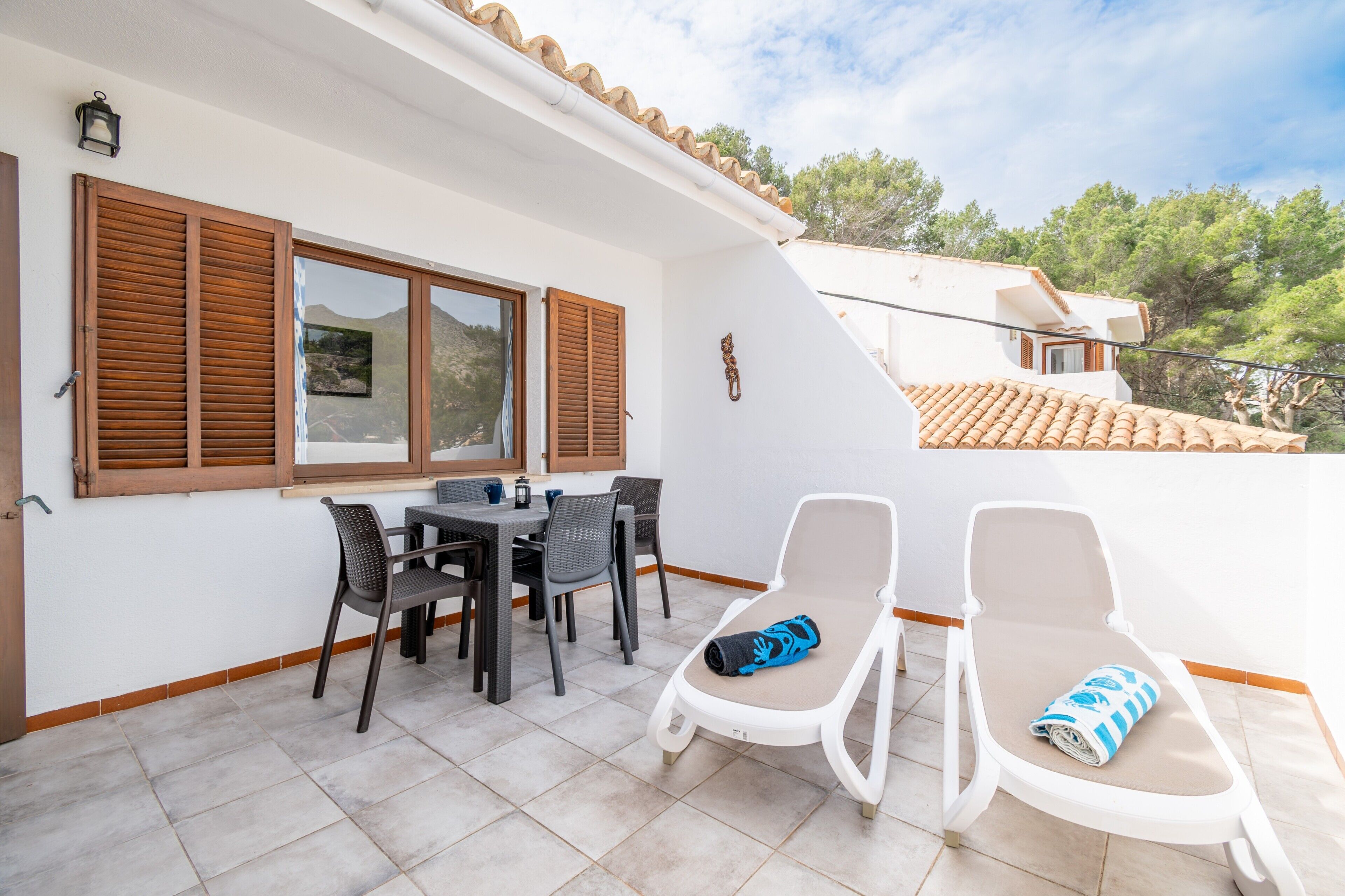 A patio with a table and chairs, a sun lounger, and a view of the surrounding landscape.
