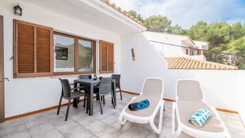A patio with a table and chairs, a sun lounger, and a view of the surrounding landscape.