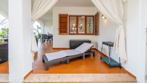Een zonnige kamer met een bed, een bankje, een tafel en een stoel.