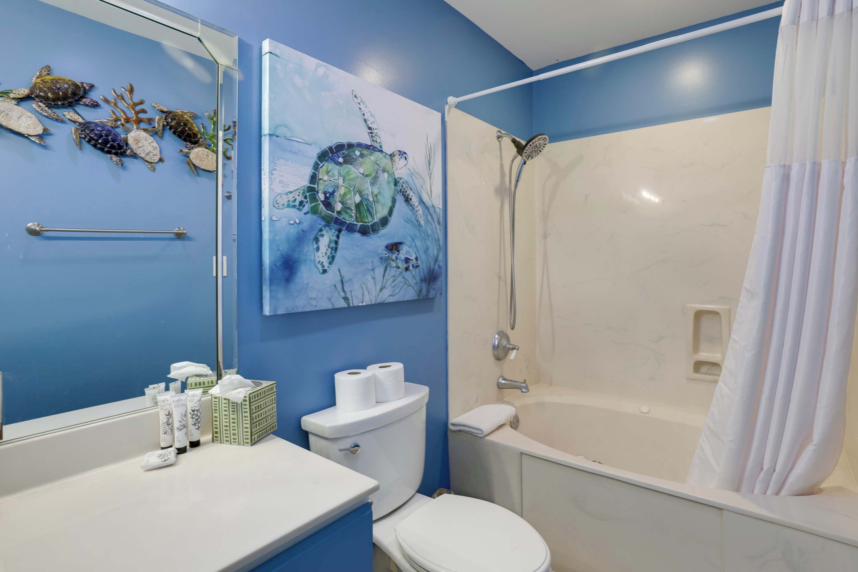 A bathroom with a white toilet, a bathtub with a showerhead, a sink with toiletries, and a large mirror.
