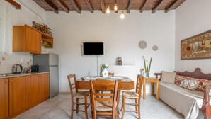 A compact kitchen with wooden cabinets, a dining table with chairs, a TV mounted on the wall, and a sofa in the living area.