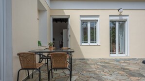 A patio with a table and chairs, stone flooring, and two windows with white frames.