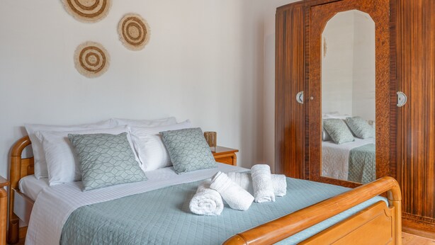 A neatly made bed with white linens and a blue quilt, a wooden wardrobe with a mirror, and three wall-mounted circular decorations.