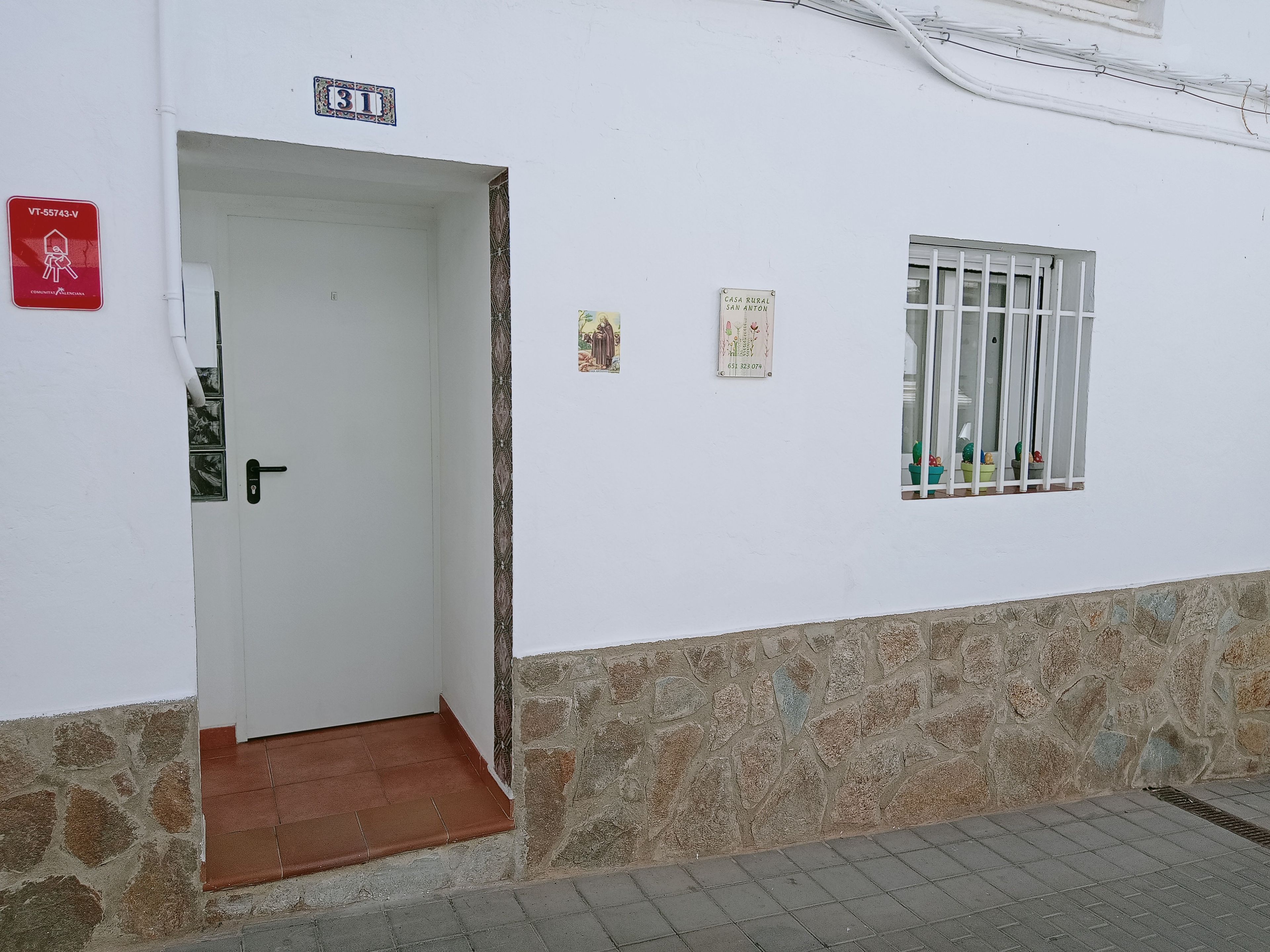 Un edificio blanco con una puerta, una ventana con barrotes y una base de piedra.