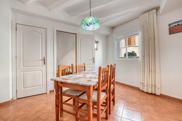 A dining area with a table and chairs, a hanging light fixture, a window with curtains, and a door. - Rural house 'Casa Rural San Antón' with mountain views (Quesa)