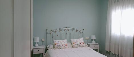 A bedroom with a bed, two bedside tables, a nightstand, a window with curtains, and a ceiling light.