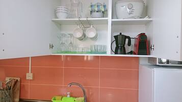 Una cucina con lavello, una macchina da caffè e diversi piatti e bicchieri sugli scaffali.