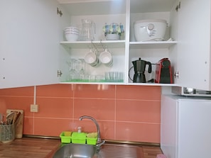 Una cocina con un fregadero, una cafetera y varios platos y vasos en estantes.