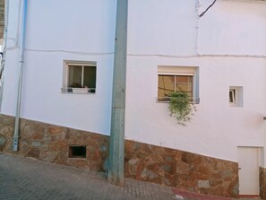 Un edificio con dos ventanas, una con balcón y una maceta, y una base de piedra.