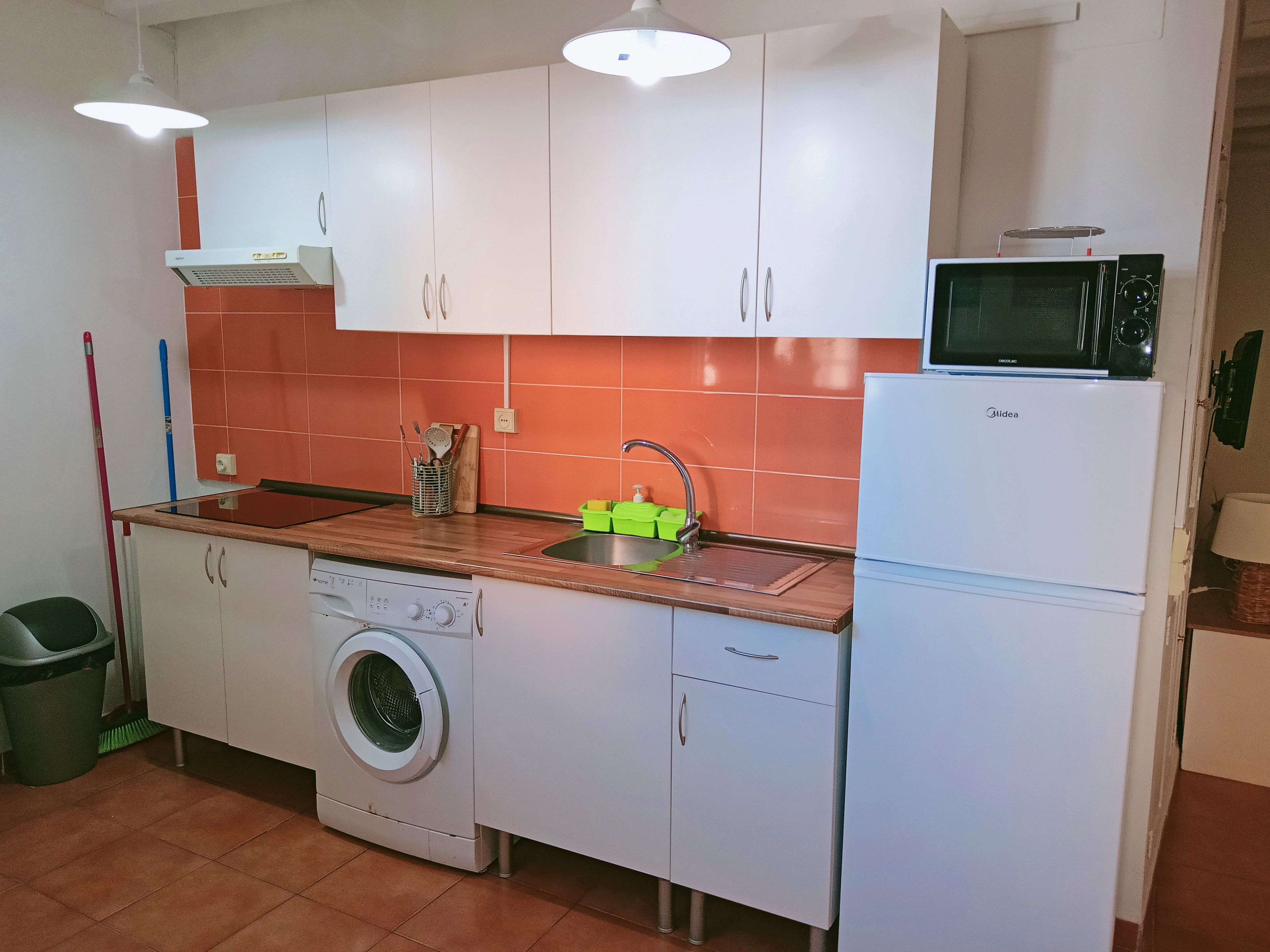 Una cocina compacta con armarios blancos, lavadora, microondas y pileta.