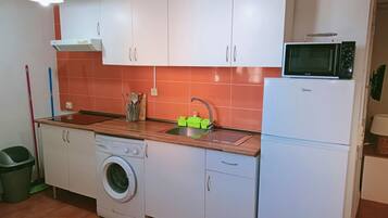 Una cocina compacta con armarios blancos, lavadora, microondas y pileta.