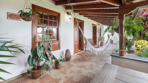Un porche cubierto con vigas de madera, plantas en macetas, una hamaca y un cartel que dice 'El patio de Tito y Julita'.