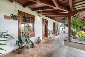 Un porche cubierto con vigas de madera, plantas en macetas, una hamaca y un cartel que dice 'El patio de Tito y Julita'.