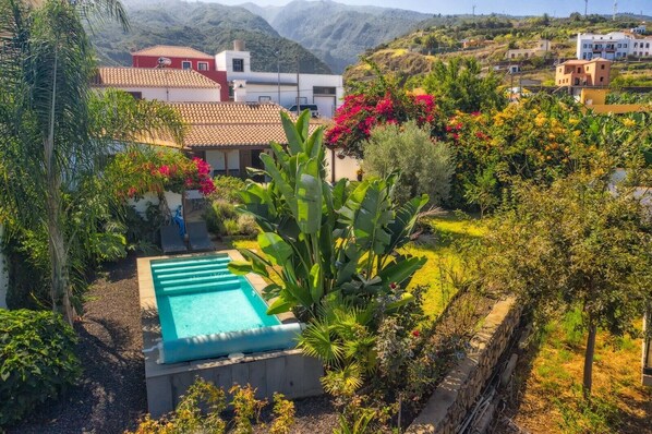 Un barrio residencial con piscina, abundante vegetación y casas con techos de tejas rojas.