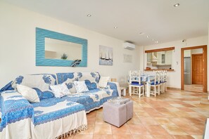 A living room with a sofa, ottoman, dining table, chairs, and a kitchen area. - Apartment 'La Casita Azul' with Shared Pool, Wi-Fi and Air Conditioning (Almuñécar)