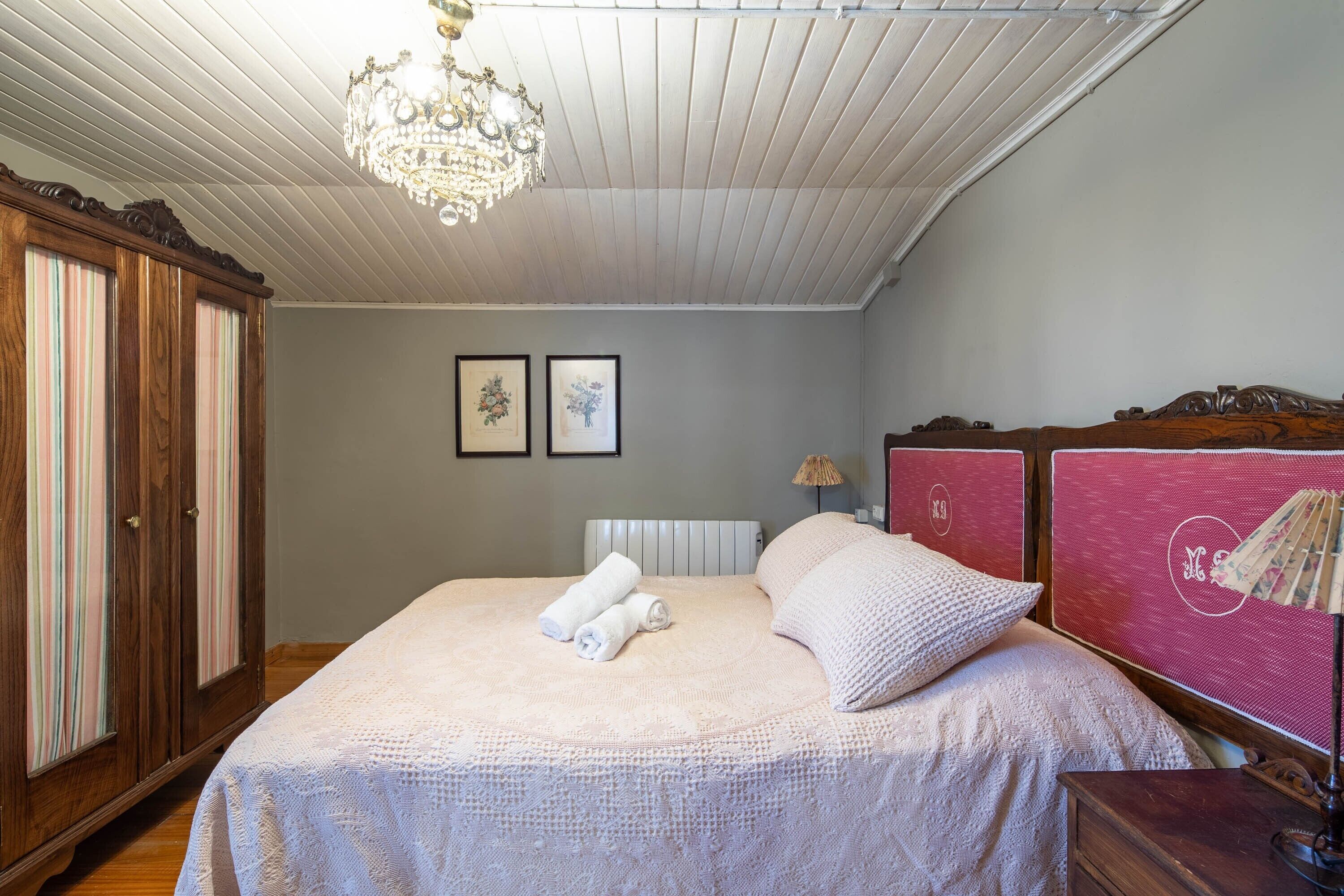 Ein Schlafzimmer mit einem Bett, einer Kandelaberleuchte, einem Kleiderschrank und zwei gerahmten Bildern an der Wand.