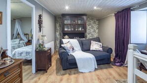 A cozy living room with a dark sofa, a cabinet with glass doors, a wooden dresser, and a bed with a canopy.