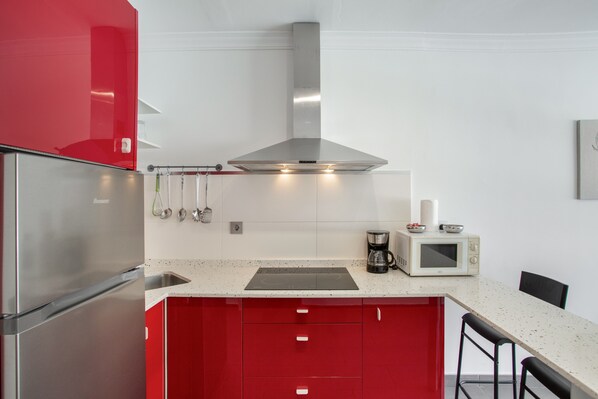 A modern kitchen with stainless steel appliances, red cabinetry, and a white countertop.