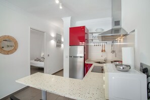 Una cocina moderna con encimeras blancas, un refrigerador rojo y una campana extractora de acero inoxidable.