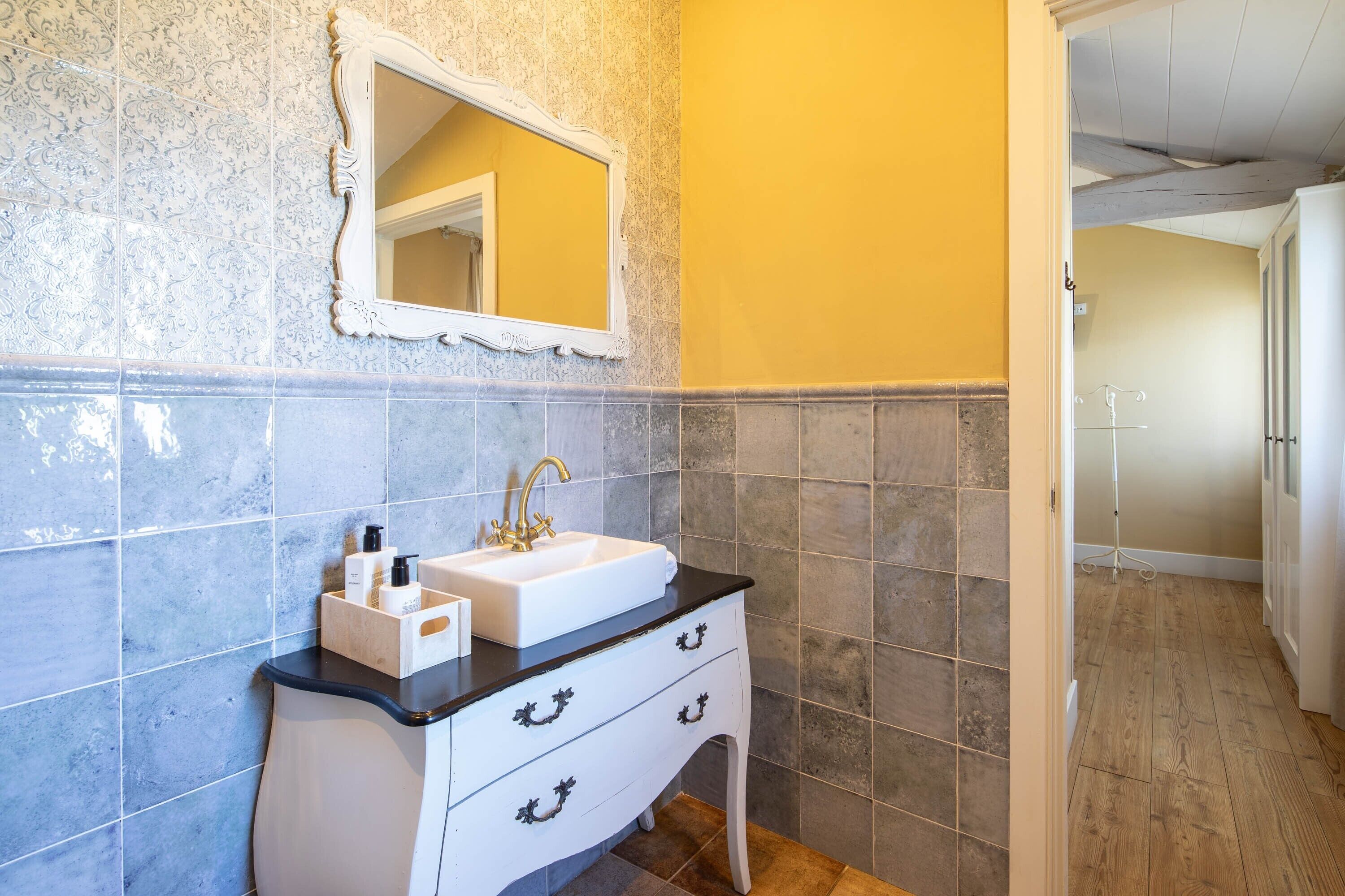 Une salle de bain avec un lavabo blanc, un miroir et un meuble-lavabo en bois.