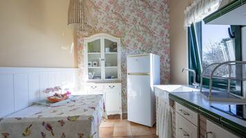 Una cocina con un refrigerador blanco, un lavamanos con ventana, un armario y una mesa con mantel floral.