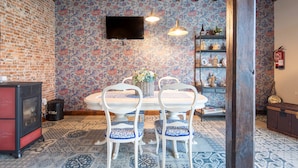 A dining area with a brick wall, patterned wallpaper, a white table, blue chairs, and a fireplace.