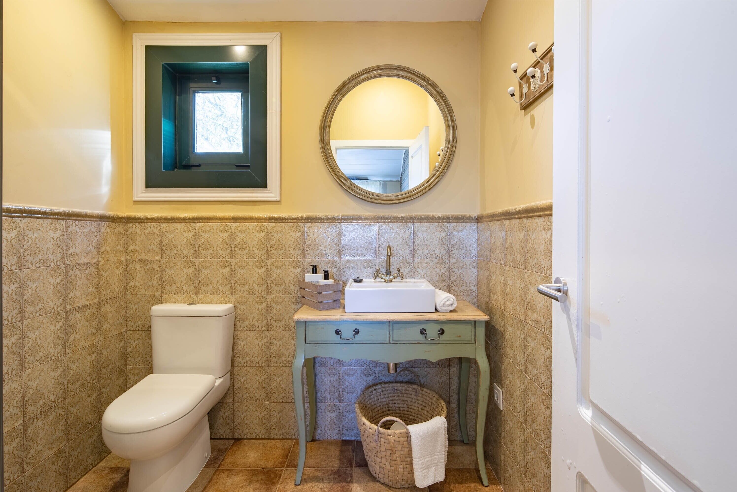 Ein Badezimmer mit Toilette, Waschbecken, Spiegel, Fenster und Handtuchhalter.