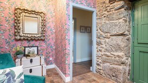Una habitación con papel tapiz floral, un espejo, una puerta verde y una pared de piedra.