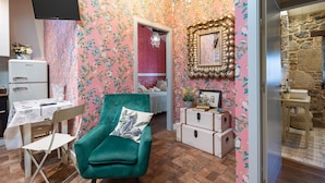 Una habitación con un sillón color turquesa, un escritorio de estilo antiguo, un aparador y un espejo en la pared.