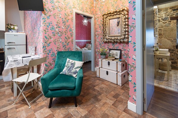 A room with a teal armchair, a vintage-style desk, a dresser, and a mirror on the wall.