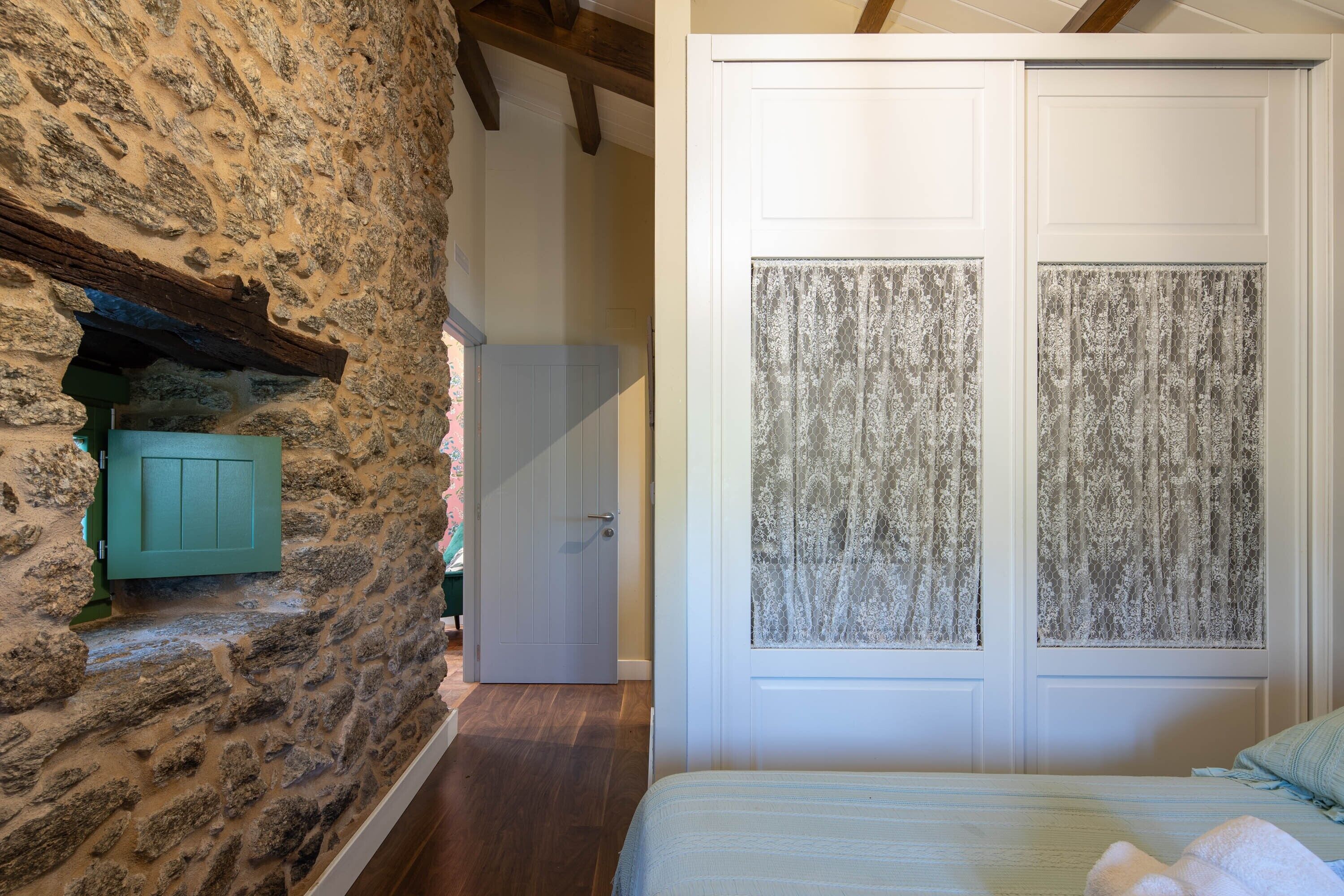 Un dormitorio con pared de piedra, cama con colcha azul y puerta blanca con paneles de vidrio esmerilado.