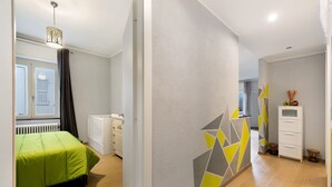 Een moderne slaapkamer met een groen bed, een radiator, een witte dressoir en een geometrisch wandontwerp.