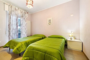 Un dormitorio con dos camas, una mesita de noche, una lámpara, una ventana con cortinas y un cuadro en la pared.