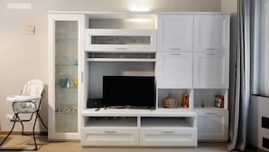 Een kamer met een witte entertainmentkast, een televisie en een babyzitje.