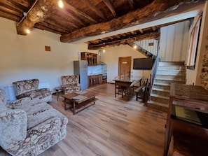 Un interior rústico con vigas de madera a la vista, comedor, cocina y escalera.