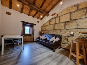 Une pièce avec un mur en pierre, un plafond en bois, un canapé avec des coussins, une table avec des chaises et un ventilateur.
