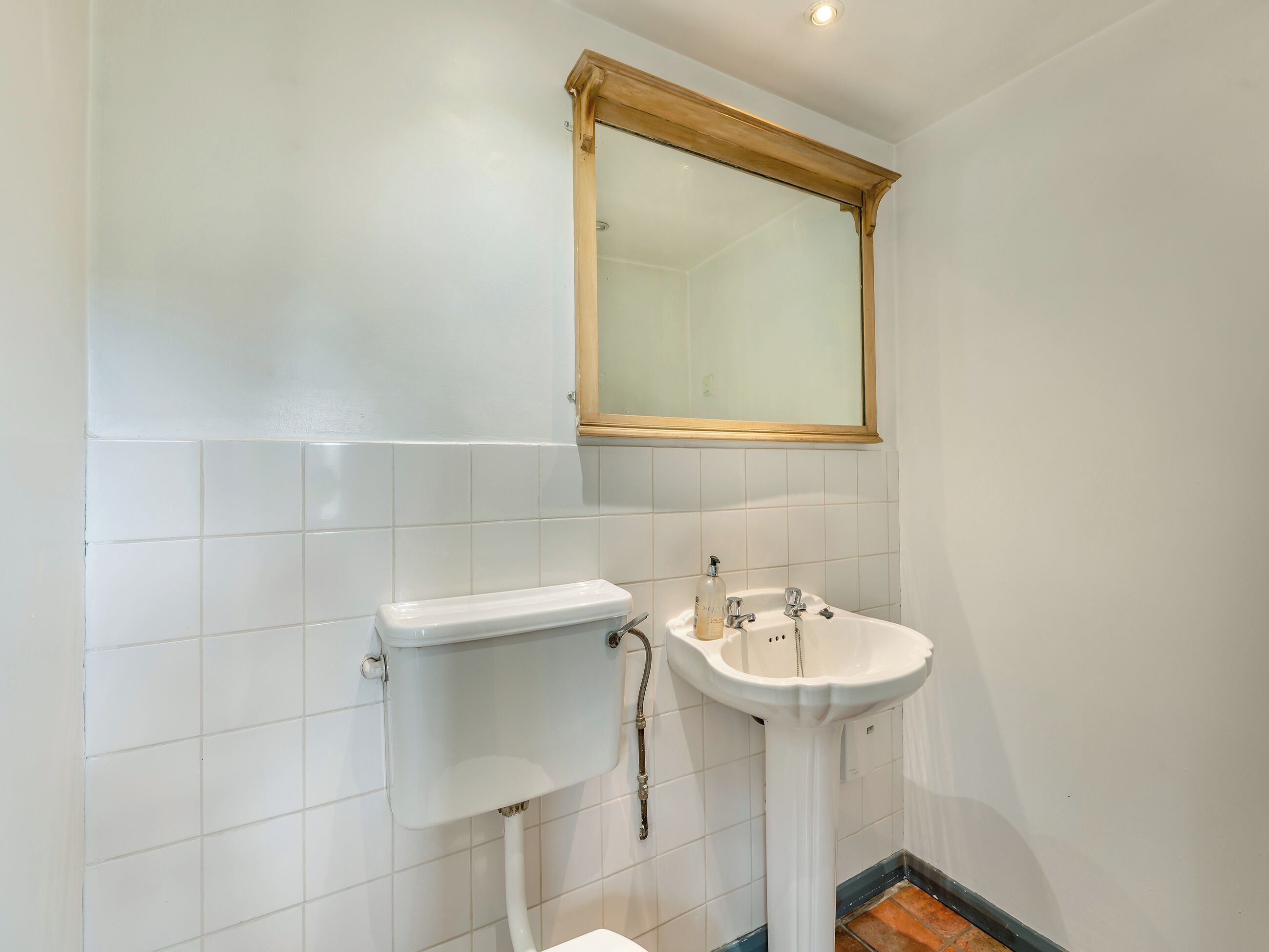 A bathroom with a white toilet, a pedestal sink, and a mirror with a wooden frame.