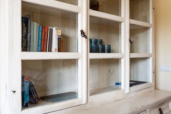 Um armário branco com portas de vidro, contendo livros e objetos decorativos.