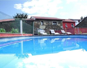 En swimmingpool med liggestole, en bygning i sten og en rød bygning i baggrunden.