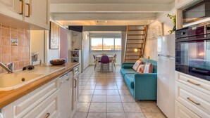 A kitchen with a dining table, a blue sofa, and a refrigerator. - Apartment 'La Conque' with Air Conditioning (Agde)