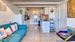 A modern kitchen with white cabinets, a central island, and a dining area with a blue sofa and patterned cushions. - Apartment 'La Conque' with Air Conditioning (Agde)