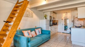 A modern kitchen with white cabinets, a blue sofa with decorative pillows, and a wooden staircase. - Apartment 'La Conque' with Air Conditioning (Agde)