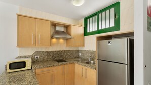 A kitchen with wooden cabinets, a stainless steel refrigerator, a microwave, and granite countertops.