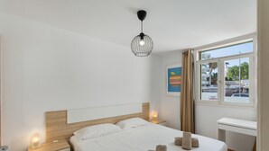 A modern hotel room with a bed, bedside tables, a desk, and a window with a view.